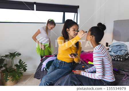 In bedroom, teen girls applying makeup and choosing outfits for celebration In bedroom, teen girls applying makeup and choosing outfits for celebration 135534979