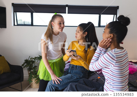 Teen girls at home laughing and chatting while using smartphone together Teen girls at home laughing and chatting while using smartphone together 135534983