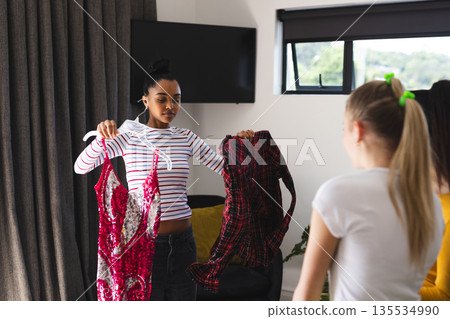 Teen girl choosing between dresses while friends offer fashion advice at home Teen girl choosing between dresses while friends offer fashion advice at home 135534990