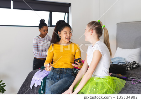 Teen girls in bedroom laughing and applying makeup, enjoying fun celebration Teen girls in bedroom laughing and applying makeup, enjoying fun celebration 135534992