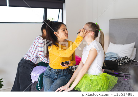 Teen girls having fun applying makeup and styling hair in bedroom 135534993