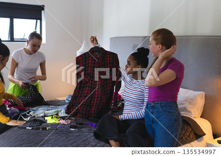 Teen girls choosing outfits together on bed, preparing for school event 135534997