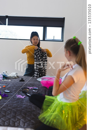 Preparing outfits for celebration, teen girls in bedroom exploring creative fashion choices 135535010