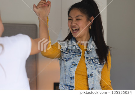 Teen girls high-fiving and laughing together at home, celebrating success Teen girls high-fiving and laughing together at home, celebrating success 135535024