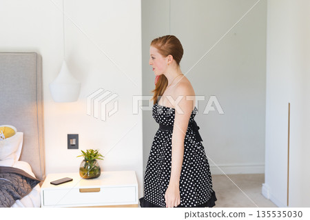 Teen in polka dot dress smiling and walking in modern bedroom Teen in polka dot dress smiling and walking in modern bedroom 135535030