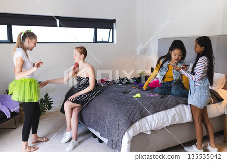 Teen girls enjoying dress-up and chatting in bedroom during fun celebration Teen girls enjoying dress-up and chatting in bedroom during fun celebration 135535042