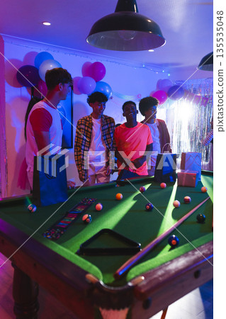 Teens celebrating around pool table with gift bags and colorful balloons Teens celebrating around pool table with gift bags and colorful balloons 135535048