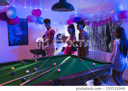 Teenagers enjoying birthday party with pool table and colorful decorations indoors Teenagers enjoying birthday party with pool table and colorful decorations indoors 135535049