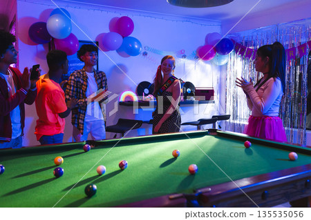 Teen friends celebrating birthday with pool table and colorful decorations at home 135535056
