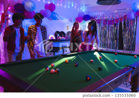 Teens enjoying birthday party playing pool in festive, colorful room with balloons Teens enjoying birthday party playing pool in festive, colorful room with balloons 135535060