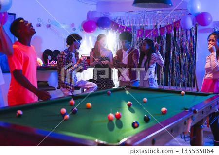 Teens celebrating birthday around pool table with balloons and decorations Teens celebrating birthday around pool table with balloons and decorations 135535064