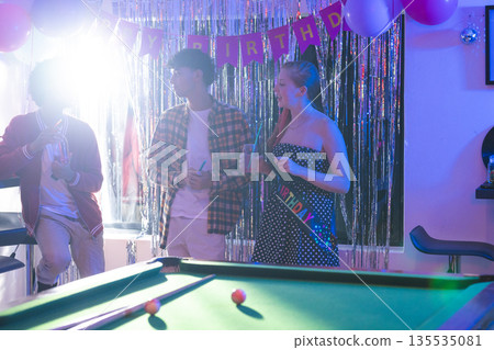 Teens celebrating birthday party with friends, enjoying drinks near pool table Teens celebrating birthday party with friends, enjoying drinks near pool table 135535081