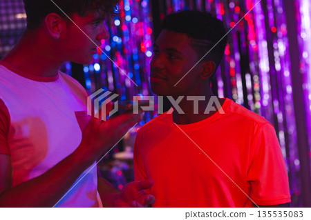 Teenagers in colorful lights at vibrant party, engaging in lively conversation Teenagers in colorful lights at vibrant party, engaging in lively conversation 135535083