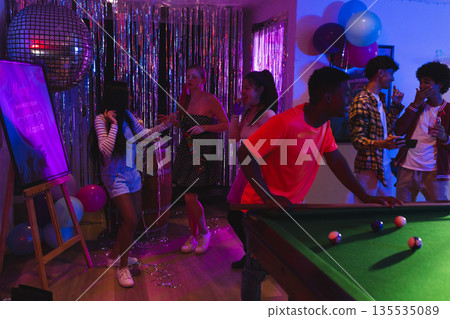 Teenagers enjoying lively dance party with pool table and colorful decorations Teenagers enjoying lively dance party with pool table and colorful decorations 135535089
