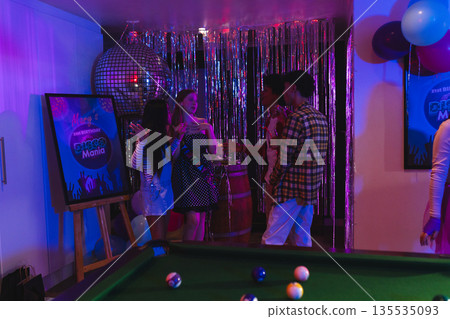 Teenagers celebrating at birthday party with pool table and disco ball decorations 135535093