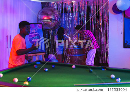 Teenagers enjoying vibrant birthday party with pool table and disco decorations Teenagers enjoying vibrant birthday party with pool table and disco decorations 135535094