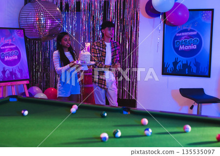 Teenagers celebrating birthday with cake and balloons at lively party 135535097