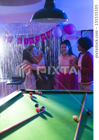 Teens celebrating birthday party, hugging and smiling near pool table with balloons 135535105