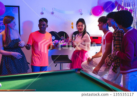 Teenagers enjoying lively party with drinks and laughter around pool table Teenagers enjoying lively party with drinks and laughter around pool table 135535117