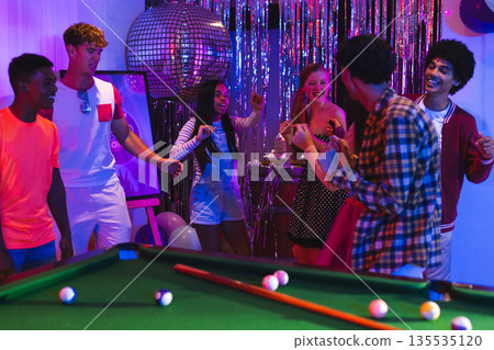 Teens celebrating around pool table with disco ball and festive decorations Teens celebrating around pool table with disco ball and festive decorations 135535120