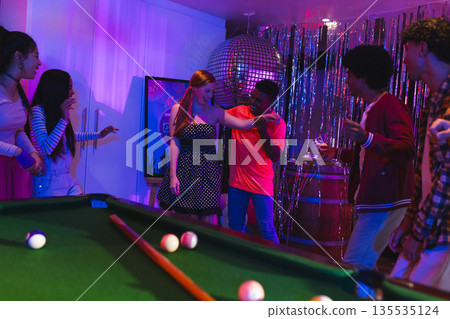 Teens celebrating at party, dancing near pool table under disco ball lights Teens celebrating at party, dancing near pool table under disco ball lights 135535124