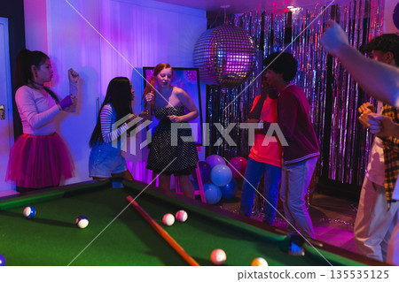 Teenagers dancing and enjoying party near pool table with disco ball lights Teenagers dancing and enjoying party near pool table with disco ball lights 135535125
