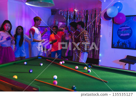 Teens enjoying lively birthday party with pool table and disco decorations 135535127