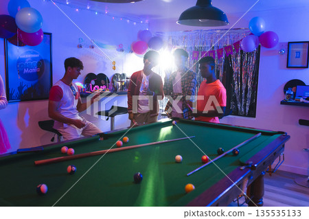 Celebrating birthday, teenagers playing pool in festive room with balloons and decorations Celebrating birthday, teenagers playing pool in festive room with balloons and decorations 135535133