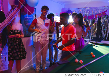 Teens celebrating birthday party with pool table and colorful decorations indoors Teens celebrating birthday party with pool table and colorful decorations indoors 135535140