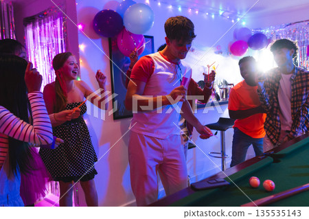 Teenagers celebrating at home, playing pool and dancing with colorful balloons 135535143