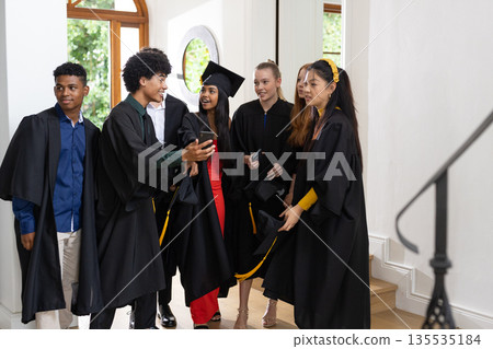 Graduating students in caps and gowns celebrating together indoors with excitement Graduating students in caps and gowns celebrating together indoors with excitement 135535184