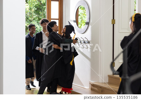 Graduates in caps and gowns celebrating with joyful hugs at home entrance Graduates in caps and gowns celebrating with joyful hugs at home entrance 135535186