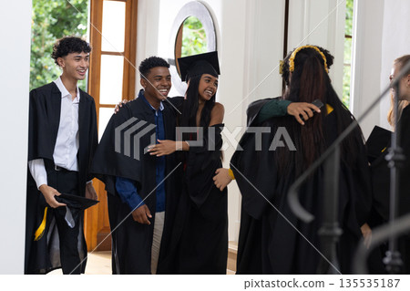 Graduating students in school wearing caps and gowns, sharing joyful hugs 135535187