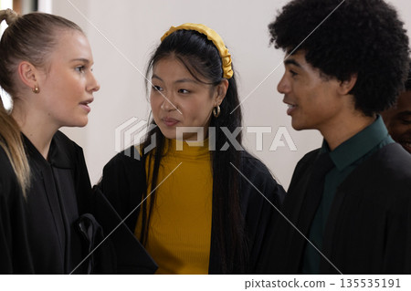 Teens in graduation gowns celebrating together, smiling and chatting happily 135535191