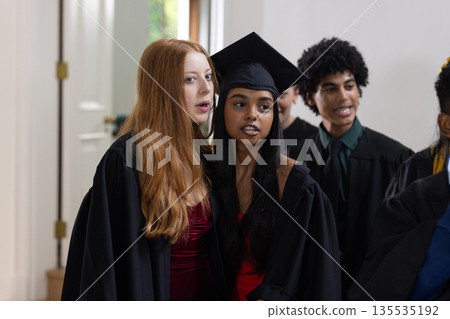 Teen graduates in caps and gowns celebrating together at school ceremony 135535192
