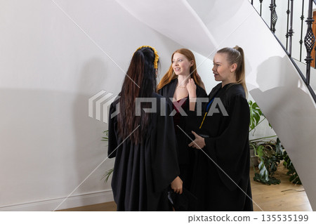 Teen graduates in gowns celebrating and chatting happily at school ceremony 135535199