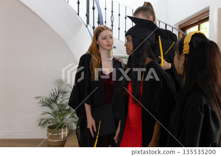 Graduating students in caps and gowns celebrating together at home Graduating students in caps and gowns celebrating together at home 135535200