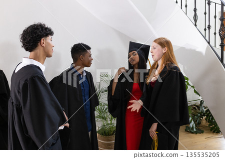 Graduating students in caps and gowns celebrating and chatting together indoors Graduating students in caps and gowns celebrating and chatting together indoors 135535205
