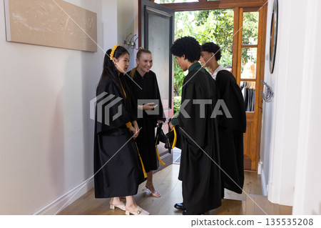 Graduating students in caps and gowns celebrating together at home entrance Graduating students in caps and gowns celebrating together at home entrance 135535208