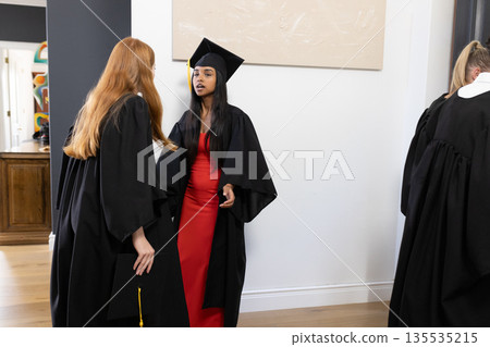 Graduates in caps and gowns chatting excitedly at home after ceremony 135535215