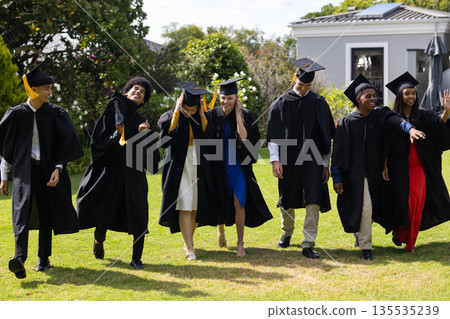 Graduating students in caps and gowns celebrating joyfully outdoors together 135535239