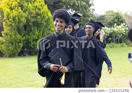 Graduating students in caps and gowns walking joyfully on green lawn Graduating students in caps and gowns walking joyfully on green lawn 135535248
