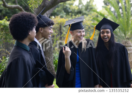 Graduating students in caps and gowns celebrating joyfully outdoors together 135535252