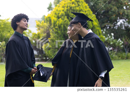 Graduating students in caps and gowns celebrating together in outdoor garden Graduating students in caps and gowns celebrating together in outdoor garden 135535261