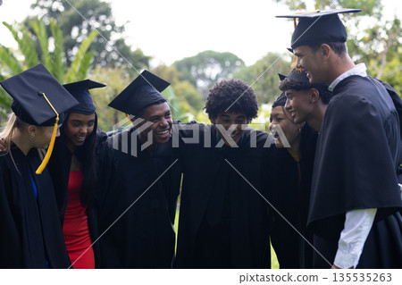 Graduating students in caps and gowns celebrating together outdoors, smiling happily 135535263