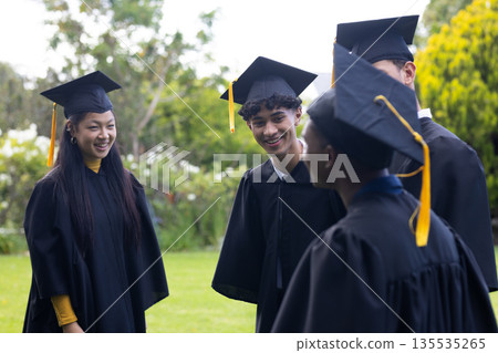 Graduating students in caps and gowns celebrating together outdoors with smiles 135535265