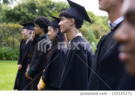 Graduating students in caps and gowns standing outdoors, smiling and celebrating 135535271