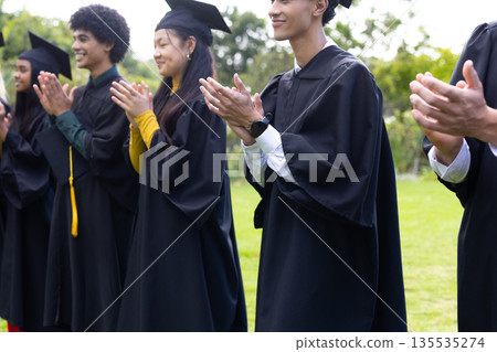 Graduating students in caps and gowns clapping outdoors, celebrating achievement Graduating students in caps and gowns clapping outdoors, celebrating achievement 135535274