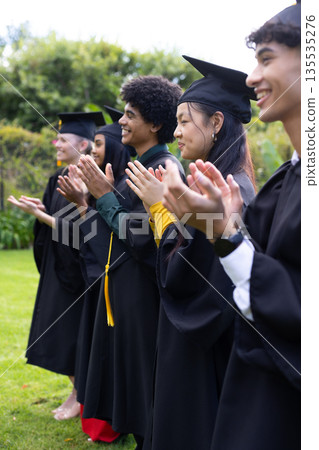 Graduating students in caps and gowns clapping joyfully at outdoor ceremony Graduating students in caps and gowns clapping joyfully at outdoor ceremony 135535276