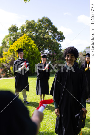 Graduating students in caps and gowns celebrating outdoors with diplomas 135535279
